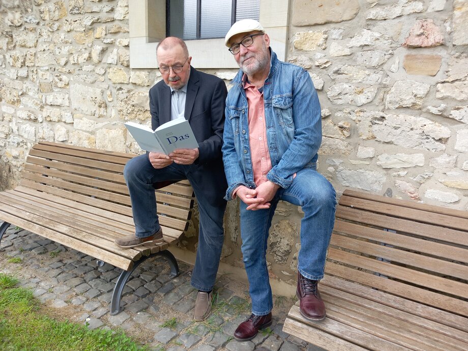 Das Bild zeigt Reinhard Försterling und Martin Krüger-Düsenberg vor einer Steinfassade, beide haben ihre Füße jeweils auf eine Bank gestellt.